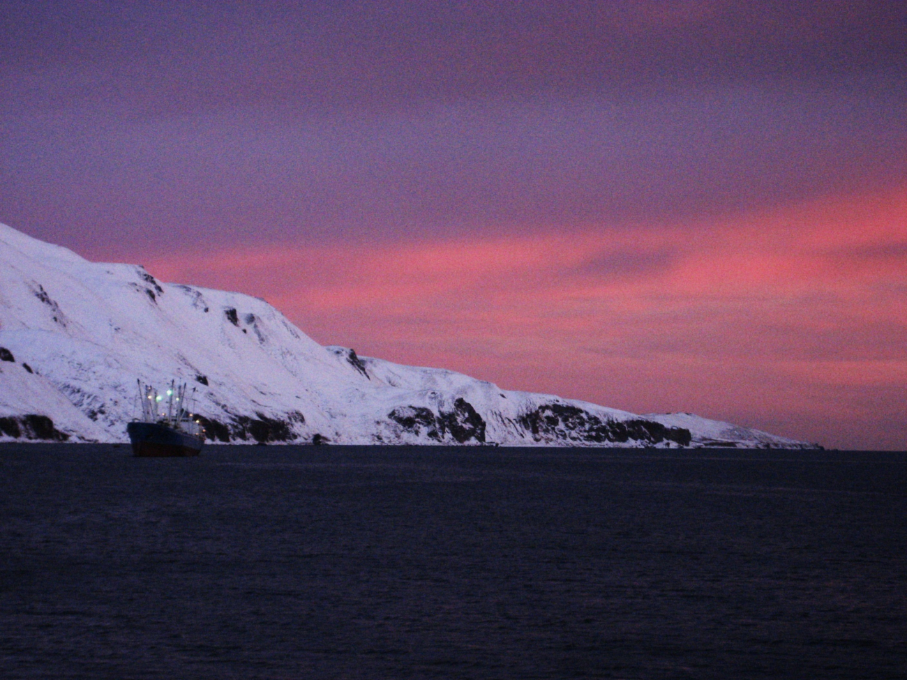 Pink glow of sunset on a winter evening with small freighter anchored out