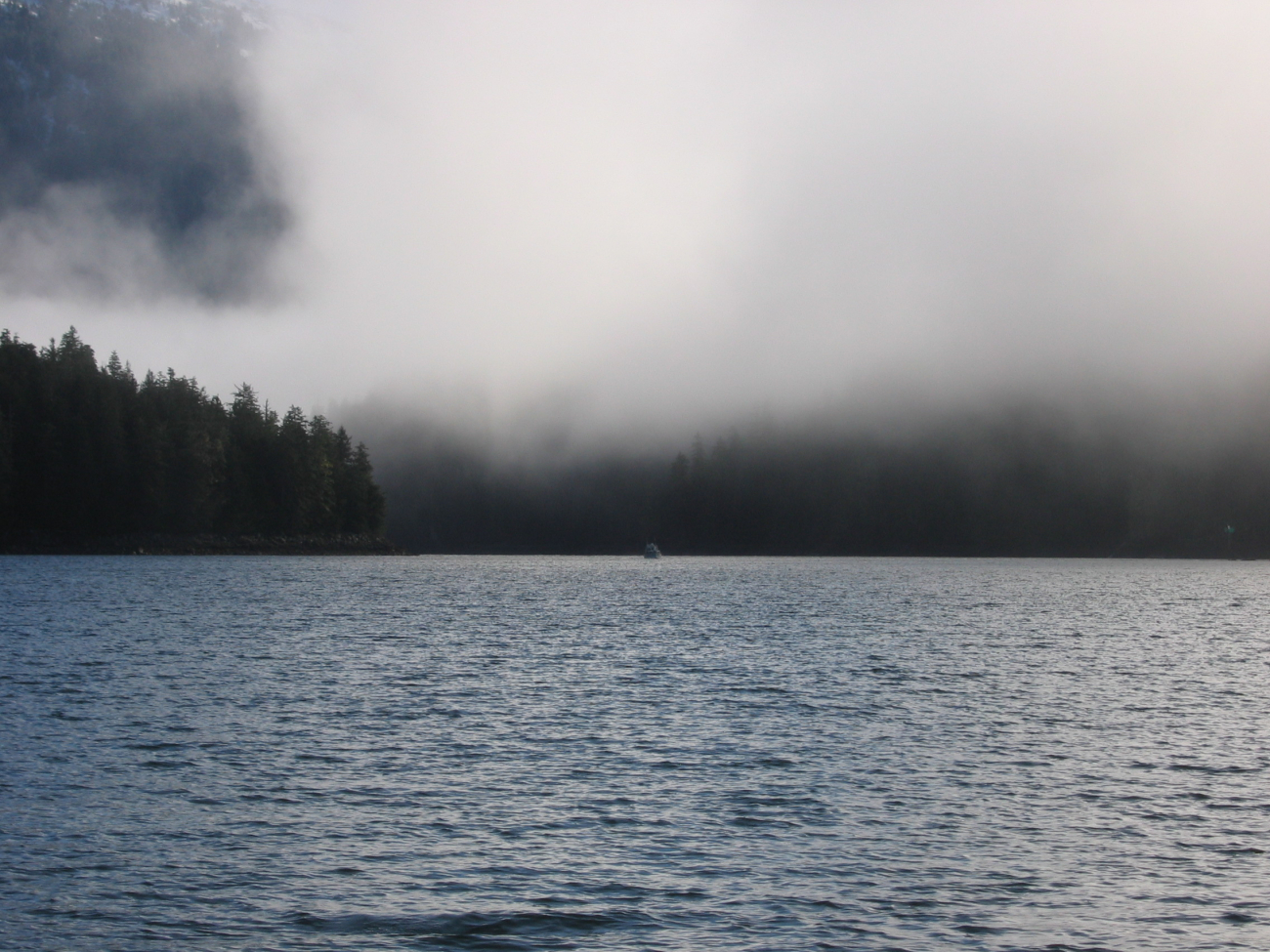 A sounding boat is seen in the distance below fog shrouded hills (Image credit: Crew and Officers of NOAA Ship FAIRWEATHER) A sounding boat is seen in the distance below fog shrouded hills