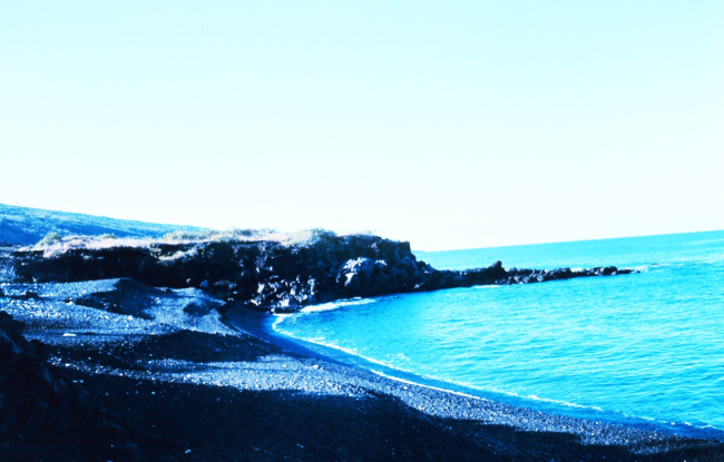 An arcuate cobble beach with a small volcanic rock outcrop at the end of thebeach
