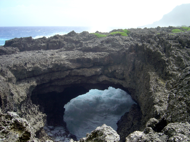 Roaring surf seen through a beautiful natural stone arch on the coast of Guam