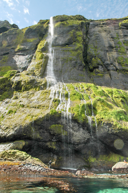 A beautiful waterfall flowing over moss-covered rocks to a kelp forest